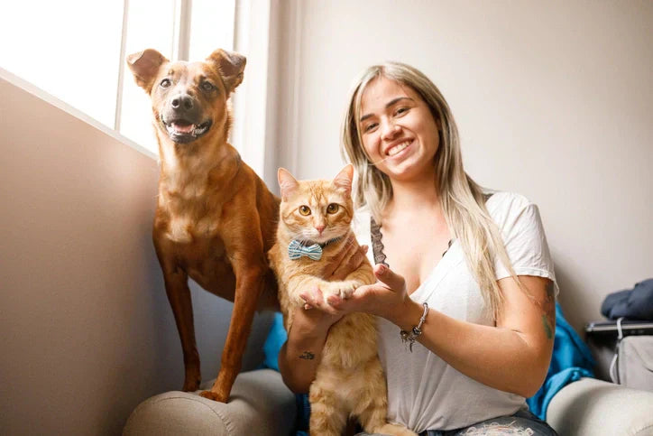  A woman sits on a couch with a dog and cat, showcasing the benefits of adopting pets for companionship and happiness.